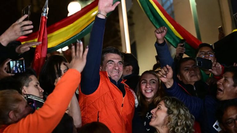 "Rodrigo Paz, presidente de Bolivia al momento de ganar las elecciones. Se encuentra en el medio de la imágen sonriendo y saludando con el brazo en alto. A su alrededor se pueden ver guirnaldas de la bandera de Bolivia y gente sonriendole"